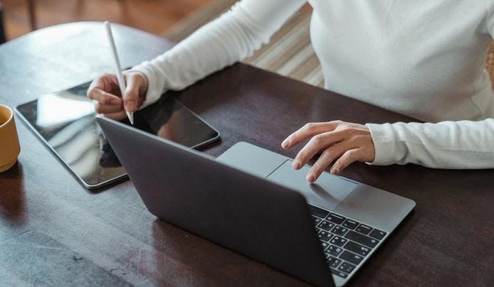 an image of a person drawing on a tablet and looking at the laptop